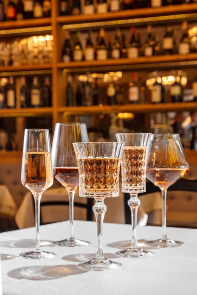 Glasses with rose wine. On a table with a light tablecloth are five glasses of different shapes and sizes with rose wine. A wine cellar is visible in the background.