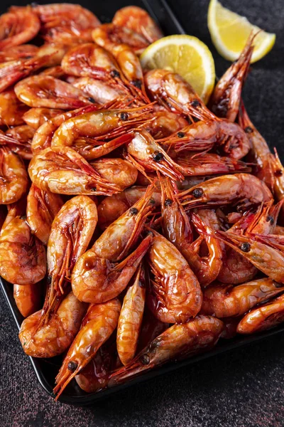 Limonlu ve maydanozlu haşlanmış karidesler koyu mavi bir zemin üzerinde demir bir kabın üzerinde yatıyor.