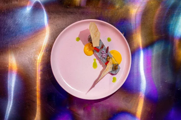 Scallop tartare with pita chips and mango sauce. Tartar lies in a round; ceramic plate; decorated with drops of balsamic. The plate stands on a metal background with a multi-colored tint. Around the plate; at a slow shutter speed; drawing with Bengal