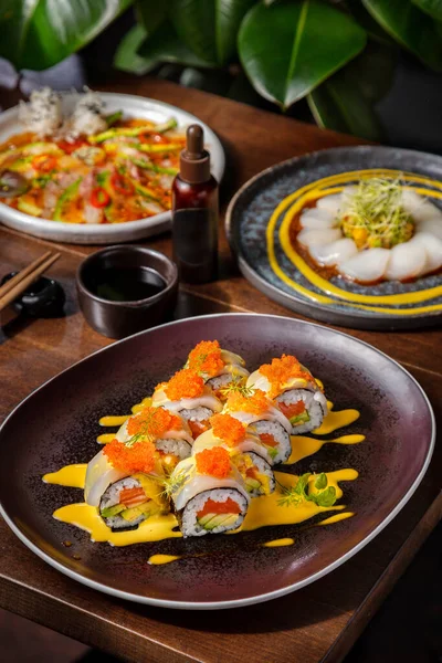 Somon, tobiko havyarı, dereotu, mürekkep balığı, avokado, pilav, nori ve soslu rulo. Masada avokado salatası, lahana, mango, peynir, mürekkep balığı ve sos ve diğer tabakta da yemek ve soya sosu var.