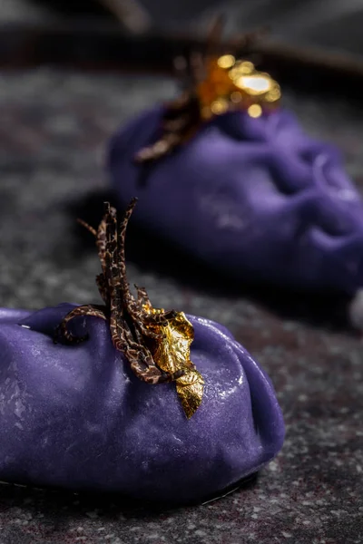Purple dumplings with truffle stripes and gold leaf in a black plate