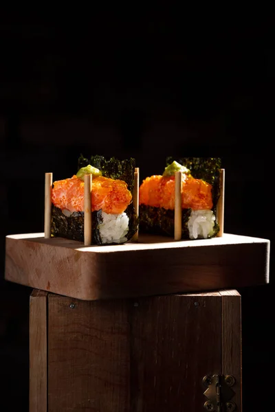 Paketlenmemiş rulo, nori, pilav, somon, sos, tobiko havyar ve wasabi ile siyah arka planda ahşap bir standda.