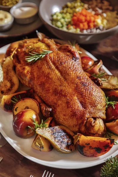 Kızarmış tavuk, armut, biberiye, elma ve ladin dalları tahta bir tabakta duruyor.