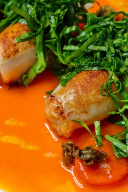 Ton balığıyla doldurulmuş mürekkep balığı ve kızarmış balık. Üstte parey var, şeritler halinde kesilmiş. Mürekkep balığı oval seramik bir tabakta, üzerine mango-chili sosu dökülüyor. Tabak bir kağıdın üzerinde duruyor, mavi arka plan..