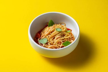 Homemade pasta with basil leaves, tomatoes and tomato sauce. Pasta lies in a light, deep ceramic plate. The plate stands on a yellow paper background.