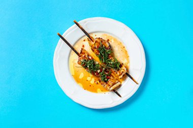 Şişte mürekkep balığı, buzdağında marul ve kırmızı biber ile birlikte mavi arka planda beyaz bir tabakta.