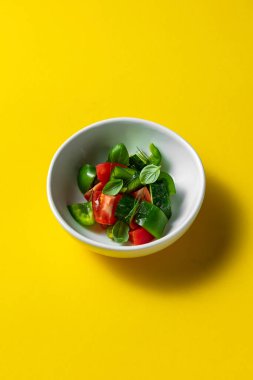 Vegetable salad of paprika, cucumber and tomato with lettuce. The food lies on a round, light, ceramic plate with a pattern. The plate stands on a yellow paper background.