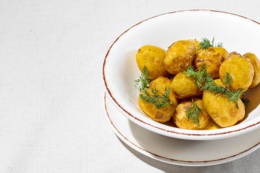 Tereyağı ve dereotlu haşlanmış patates. Patates hafif, derin, seramik bir tabakta yatıyor. Tabak tabağın üstünde. Tabaklar hafif bir keten arka planda duruyor..