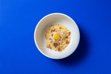 Mavi arka planda beyaz bir tabakta kremalı soslu yılan balığı ve kalamar.