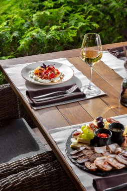 Domatesli krema. Kırmızı ve sarı domatesli tuzlu süzme peynir, kırmızı soğan, kırmızı fesleğen yaprağı ve zeytinyağı. Yemekler yuvarlak, seramik tabakta. Tabak açık renkli kumaş bir paspasın üzerinde duruyor. Çöp ahşap bir masanın üzerinde, hemen yanında. 