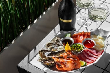 Sashimi assorted tuna, salmon, scallop, oysters, boiled shrimp. Sashimi lie on a large, ceramic, light dish in the form of an oyster shell, in the center there are metal bowls with cranberry and unagi sauces, as well as avocado tartare. The dish is o
