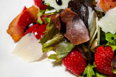 Italian dish. Salad with jamon, parmesan cheese, strawberries, arugula and lettuce leaves, balsamic sauce. The salad lies in a round, light ceramic plate. The plate stands on a light, linen background.