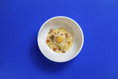 Mavi arka planda beyaz bir tabakta kremalı soslu yılan balığı ve kalamar.