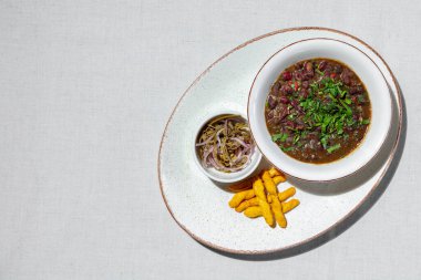 Lobio. Bitki ve bitkilerle dolu Gürcü kırmızı fasulye yemeği. Lobio yuvarlak, derin, seramik bir tabakta yatıyor. Yakınlarda gressini var ve içinde soğan ve yeşillik turşusu olan bir kase var, Lobio, gressini ve sebzeler oval seramik tabakta yatıyor. Tabak üzerinde duruyor.