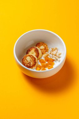 Şeftalili ve hindistan cevizli peynirli kekler sarı arka planda bir kasede.