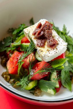 Salad with sun-dried tomatoes, feta cheese, parsley, basil and lemon in a plate on a red background