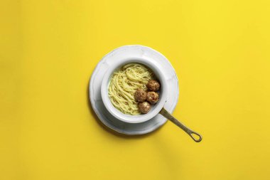 Tavşan fileto köfteli ev yapımı erişte. Yemek beyaz, seramik bir tabakta, üst tarafları ve yaldızlı bir sapı var. Tabak yuvarlak, seramik bir tabağın üzerinde duruyor. Tabaklar sarı bir kağıtta durur.