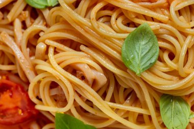 Homemade pasta with basil leaves, tomatoes and tomato sauce. Pasta lies in a light, deep ceramic plate. The plate stands on a yellow paper background.