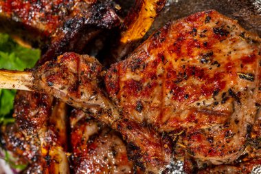 Bir parça dana eti. Kemikte üç parça dana eti var, ızgarada. Parçalar birbirinin üstünde, yanında marul ve kırmızı soğan halkalarından bir yaprak uzanıyor. Kare gümüş, yuvarlak bir tabakta yatıyor. Tabak bir ışıkta duruyor, keten arka plan..