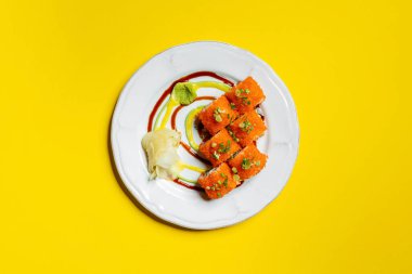 Yılan balığı, Japon mayonezi ve salatalık ile doldurulmuş suşi rulosu, pirinçle sarılmış ve kırmızı uçan balık havyarı Tobiko serpiştirilmiş yeşil soğan serpiştirilmiş. Suşi hafif, yuvarlak, seramik bir tabakta yatar. Japon mayonezi çizgileri...