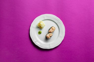 Nori 'ye sarılı pirinçle doldurulmuş iki silah ve üstüne de tartar. Nunkanlar beyaz, yuvarlak, desenli seramik bir tabakta dururlar. Yakınlarda bir kare wasabi ve turşulu zencefil var. Tabak mor bir arka planda duruyor..