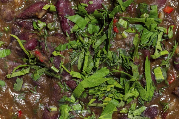 Lobio. Bitki ve bitkilerle dolu Gürcü kırmızı fasulye yemeği. Lobio yuvarlak, derin, seramik bir tabakta yatıyor. Yakınlarda gressini var ve içinde soğan ve yeşillik turşusu olan bir kase var, Lobio, gressini ve sebzeler oval seramik tabakta yatıyor. Tabak üzerinde duruyor.