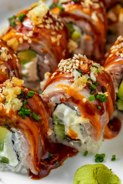 Philadelphia usulü salatalık ve Philadelphia peyniri ile doldurulmuş pilav ve füme yılan balığı filetosu. Üstü unagi soslu, susam tohumlu ve ince doğranmış yeşil soğanlı. Philadelphia suşisi yuvarlak, beyaz seramik bir tabakta yatıyor.