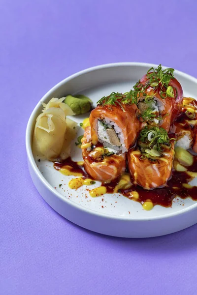 Avokado, tofu ve Philadelphia peyniri ile doldurulmuş, somon balığına sarılı, unagi soslu, ince doğranmış yeşil soğan ve limonlu. Suşi beyaz, yuvarlak, seramik bir tabağın üzerinde duruyor, yanında da turşulu g var.