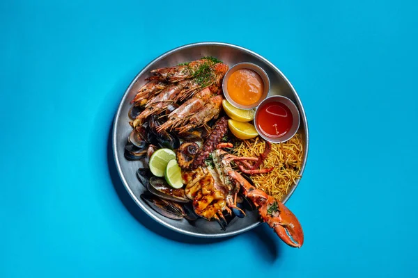 Metal bir tepside ızgara deniz mahsulleri bulunur. Kaplan karidesleri, ahtapot, ıstakoz, midye ve patates cipsi, yanında acı biber soslu ve ketçaplı iki metal fincan tabağı, iki misket limonu ve ince dilimlenmiş dereotu serpiştirilmiş. Tepsi hareket halinde.