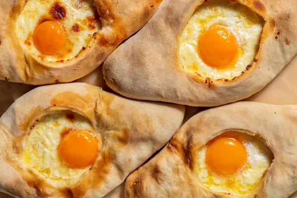 İçinde eritilmiş süluguni peyniri ve çiğ yumurta sarısı olan dört Gürcü Adjarian Khachapuris. Khachapuri odun ateşinde pişiyor. Khachapuri kahverengi parşömen üzerinde uzanıyor..