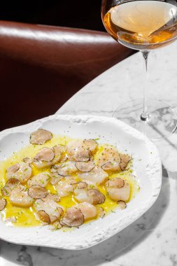 Mantarlı mantar dilimleri ve zeytinyağı ve bitkilerle karides carpaccio. Yakınlarda bir bardak köpüklü şarap ve bir şişe şarap var. Mermer tezgahta seramik tabakta yemek.. 