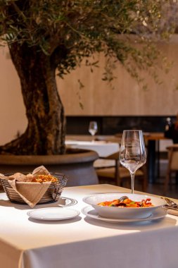 Hafif seramik tabakta deniz mahsullü domates çorbası. Çorba, yanında hafif masa örtüsü olan bir masanın üzerinde kırmızı şarap ve çatal bıçak takımı var..