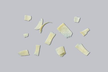 Farklı şekil ve boyutlarda parmesan peyniri dilimleri gri arka planda yatar..