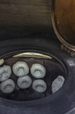 In a large tandoor oven, various Caucasian breads are laid out along the walls for baking.