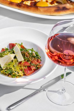 Vegetable tabbouleh with goat cheese. herbs and herbs in a light ceramic plate on a white tablecloth. Nearby is a glass of rose wine and plates with cutlery.