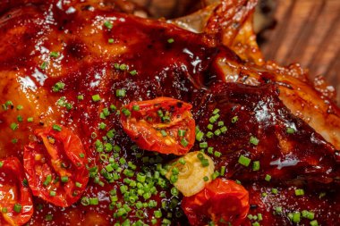 A whole leg of lamb roasted on a fire and in teriyaki sauce with fried tomatoes lies on a wooden board. Nearby are bowls of potatoes and a creamy sauce with olive oil.