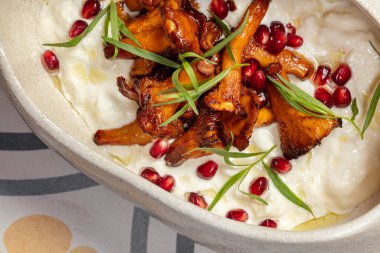 Dumplings in sour cream with fried chanterelle mushrooms and finely chopped greens in a light, ceramic plate with high sides.