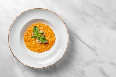 Italian dish risotto with cheddar cheese and grilled scallop, with basil leaves on top. Food in a light ceramic plate with wide margins on a marble background.