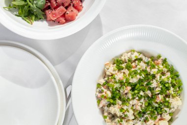 Salad Olivier with smoked chicken and boiled chicken in a light ceramic plate on a white tablecloth.