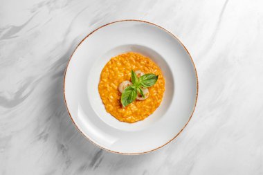 Italian dish risotto with cheddar cheese and grilled scallop, with basil leaves on top. Food in a light ceramic plate with wide margins on a marble background.