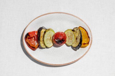 Grilled vegetables. Grilled paprika, eggplant, tomato and zucchini. Food lies on a light ceramic plate on a light tablecloth.