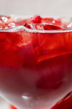 Pomegranate Spritz. Cocktail in a tall glass goblet with ice cubes and pomegranate. Nearby are pieces of a whole pomegranate. The glass stands on a light tablecloth.