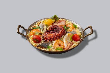 Ahtapot, levrek, mürekkep balığı ve sata soslu kiraz domatesli bir makarna. Yiyecekler gri arka planda sapları olan metal bir kasede yatıyor..