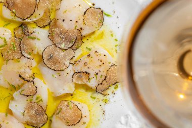 Mantarlı mantar dilimleri ve zeytinyağı ve bitkilerle karides carpaccio. Yakınlarda bir bardak köpüklü şarap ve bir şişe şarap var. Mermer tezgahta seramik tabakta yemek.. 