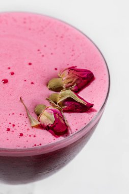 Vermouth with raspberry foam and rosebuds. A drink in a glass with a high stem. stands on a light linen fabric.