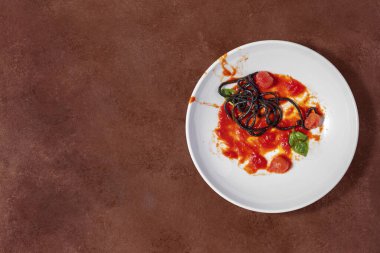 Spaghetti with cuttlefish ink, cherry tomatoes, basil leaves and grilled octopus. The food lies in a light ceramic plate and stands on a brown, stone background. Nearby are saucepans with sauce and pasta.