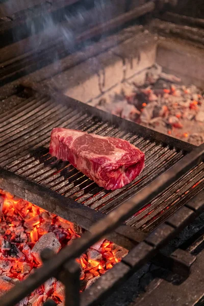 A piece of New York beef steak is fried on a grill on a grill grate. From below you can see hot coals, fire and smoke.