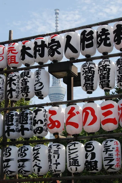 Kırmızı ve siyah Japon karakterlerin arka planda televizyon kulesi var.