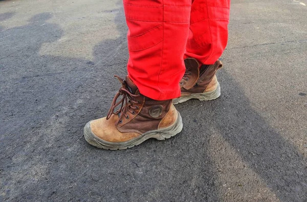 The lower of the feet of a healthy safety and environmental officer who wears a red uniform (pants) and brown safety shoes.