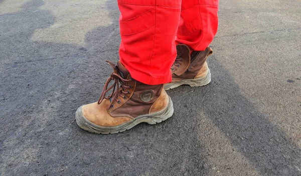 The lower of the feet of a healthy safety and environmental officer who wears a red uniform (pants) and brown safety shoes.